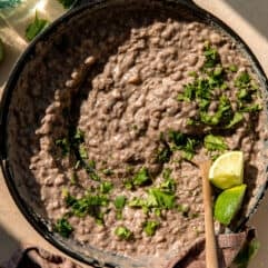 Skillet filled with refried beans, topped with cilantro and lime wedges.