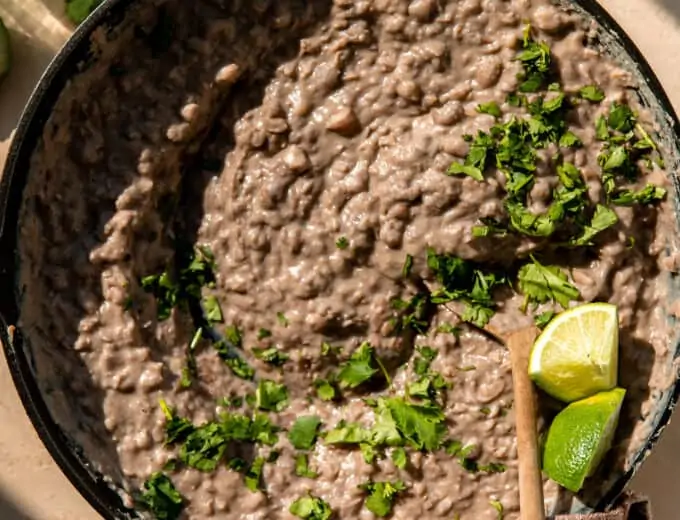 Skillet filled with refried beans, topped with cilantro and lime wedges.