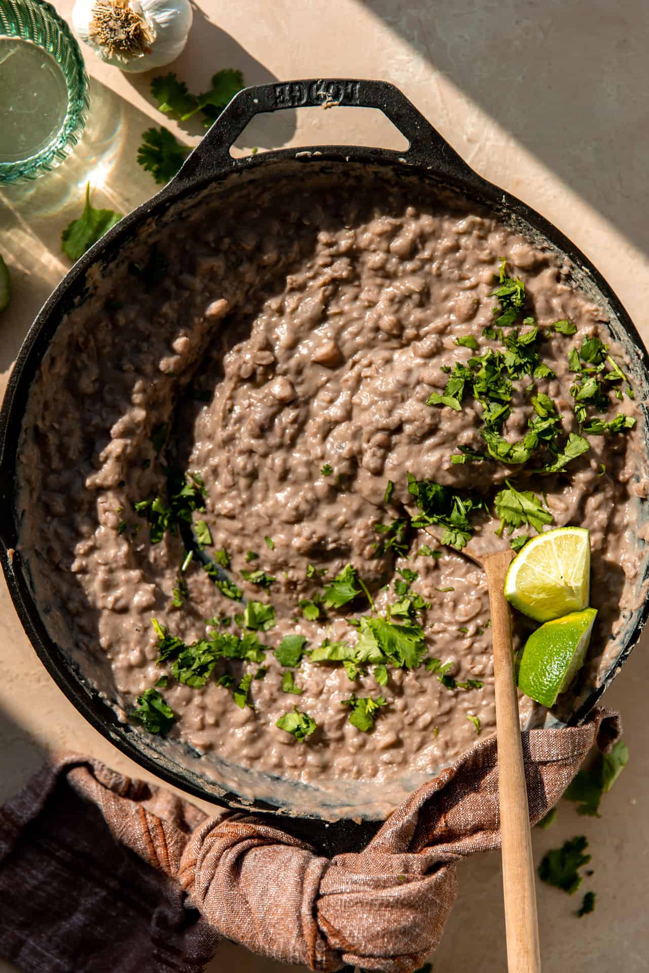Skillet filled with refried beans, topped with cilantro and lime wedges. 