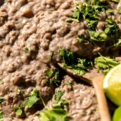 Spoon scooping up thick and creamy refried beans topped with cilantro and lime wedges.