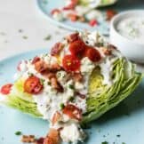 Wedge of lettuce on a blue plate topped with blue cheese dressing, tomatoes, bacon and chives.