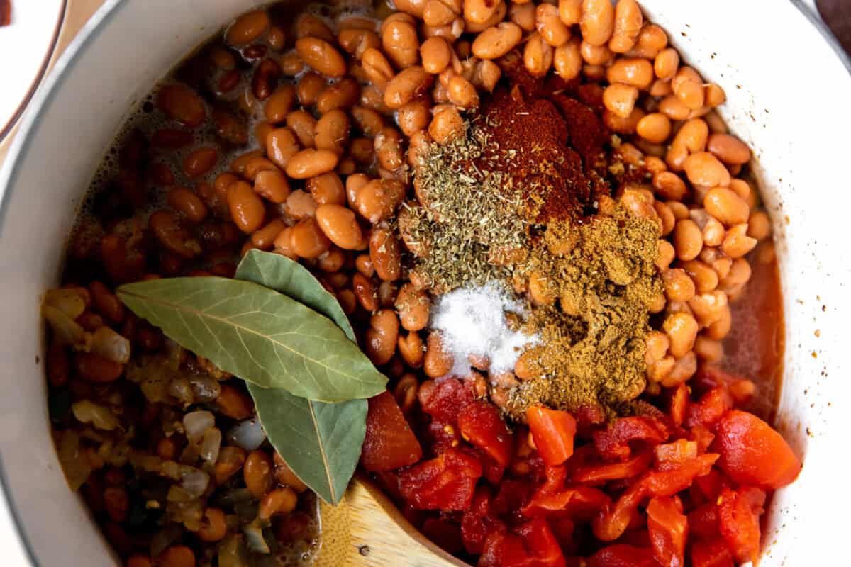 Beans, seasonings, tomato, bay leaves added to a dutch oven for making borracho beans.