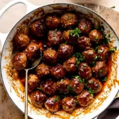 White skillet filled with bacon bourbon meatballs and topped with fresh parsley.