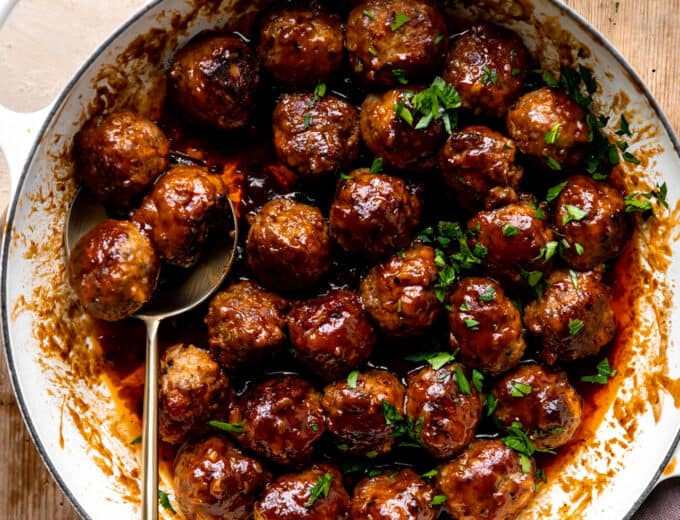 White skillet filled with bacon bourbon meatballs and topped with fresh parsley.
