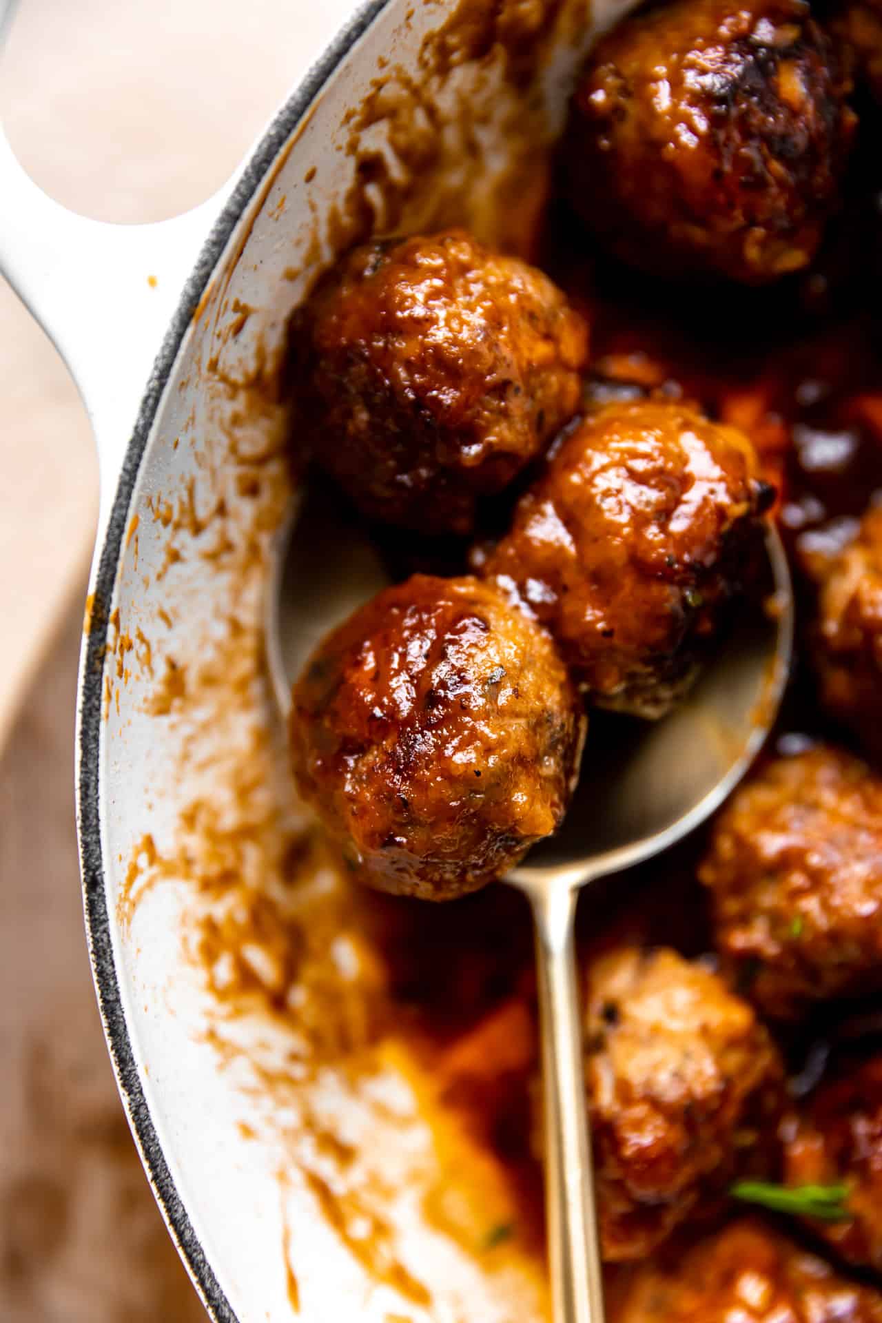 Spoon serving up cooked bacon meatballs in a bourbon BBQ sauce.