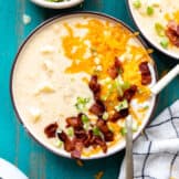 Bowl of potato soup topped with melted cheddar cheese, sour cream, diced bacon and green onion.