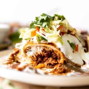 Wet burrito cut open to show it's filled with ground beef, cheese and rice. Topped with red sauce and sour cream.