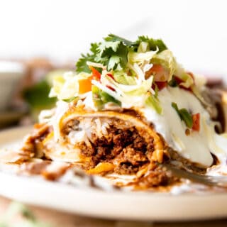Wet burrito cut open to show it's filled with ground beef, cheese and rice. Topped with red sauce and sour cream.