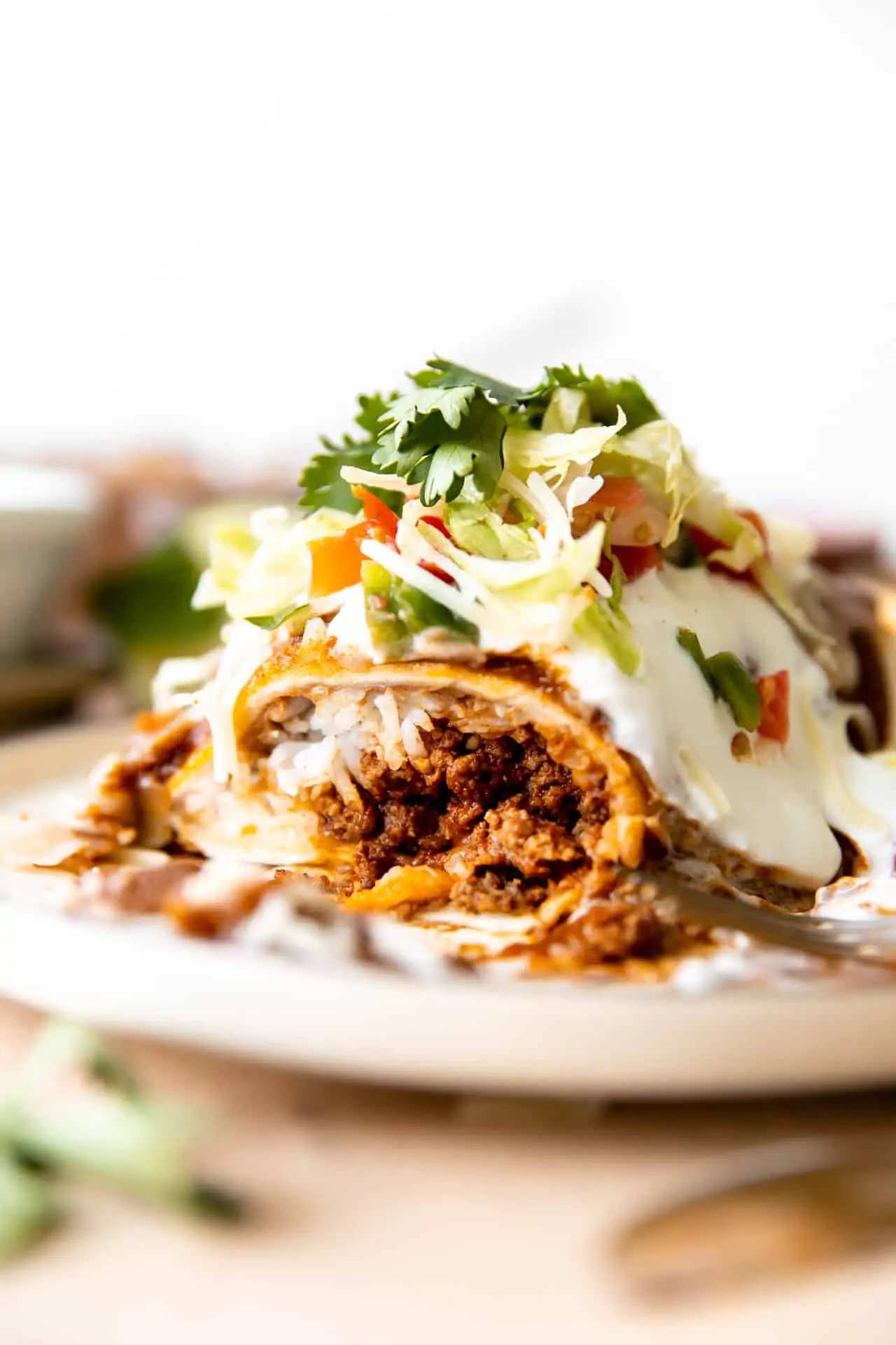 Wet burrito cut open to show it's filled with ground beef, cheese and rice. Topped with red sauce and sour cream. 