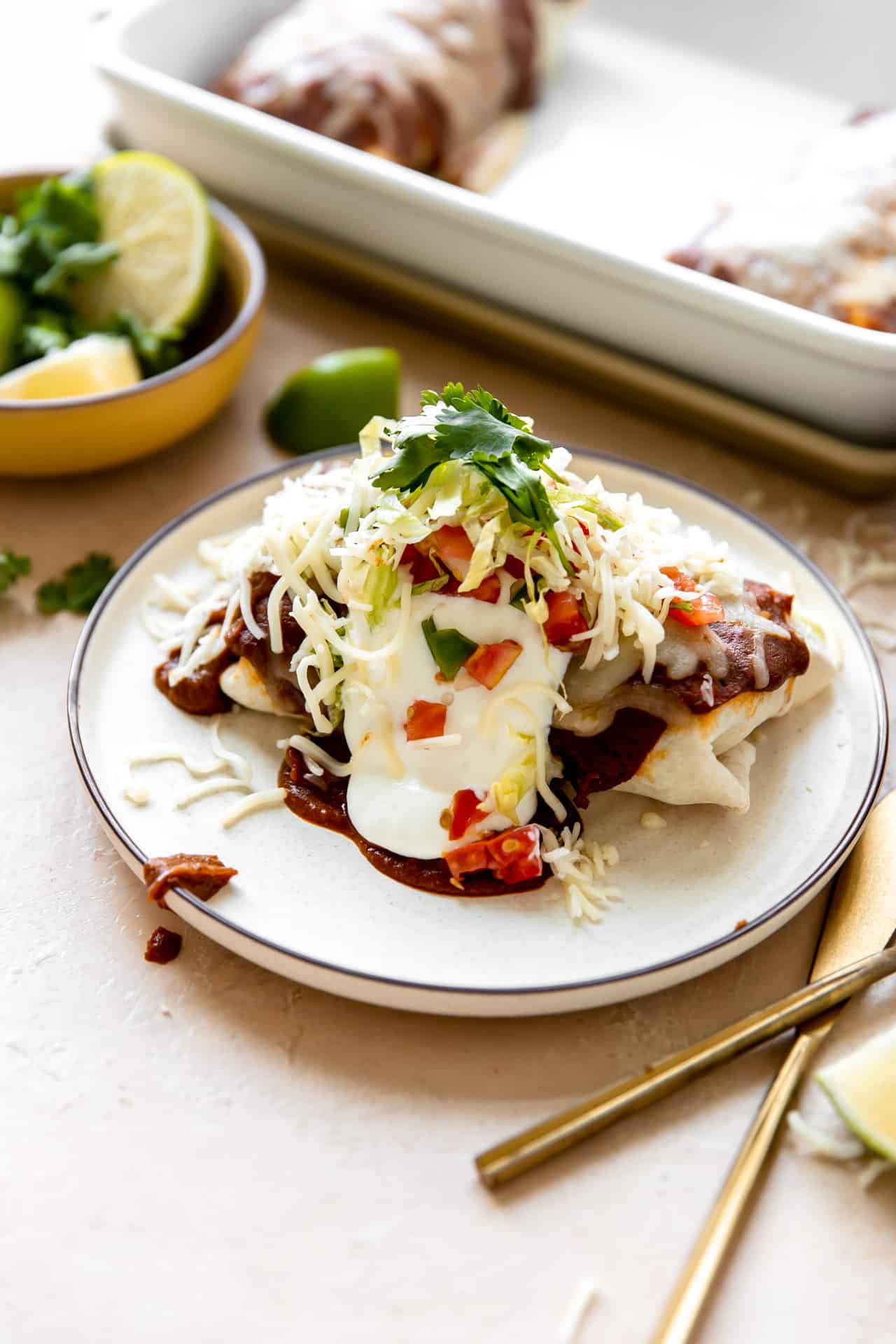 Finished dish, smothered burrito served on a plate and topped with sour cream, fresh lettuce, tomato and cilantro.