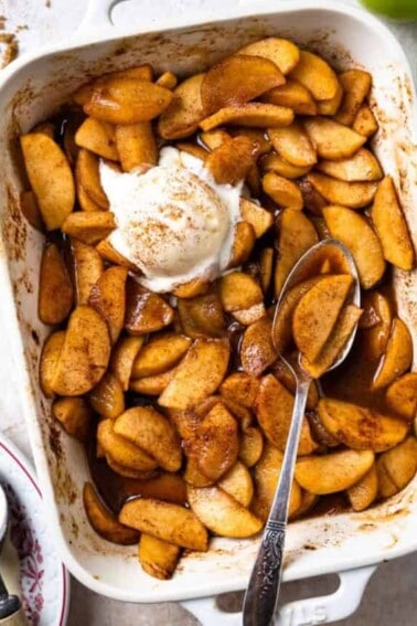 Baking dish filled with baked apples swimming in a cinnamon spiced syrup and topped with vanilla ice cream.