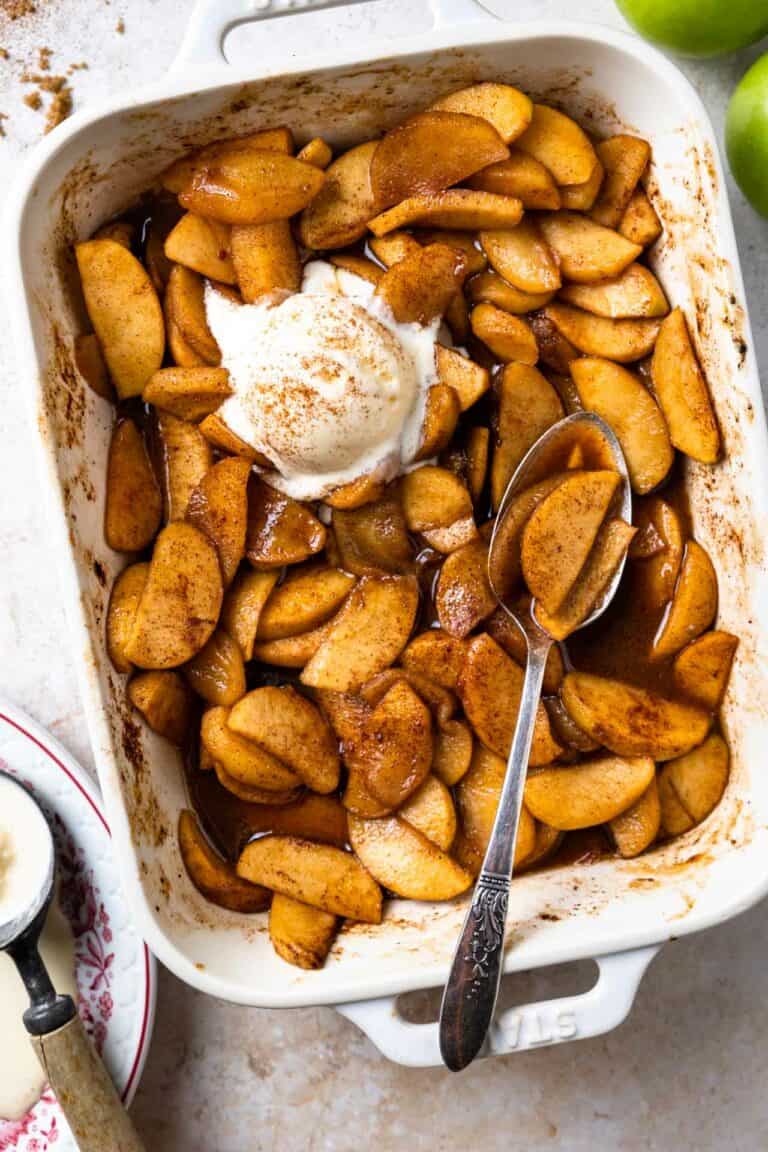 Baking dish filled with baked apples swimming in a cinnamon spiced syrup and topped with vanilla ice cream.