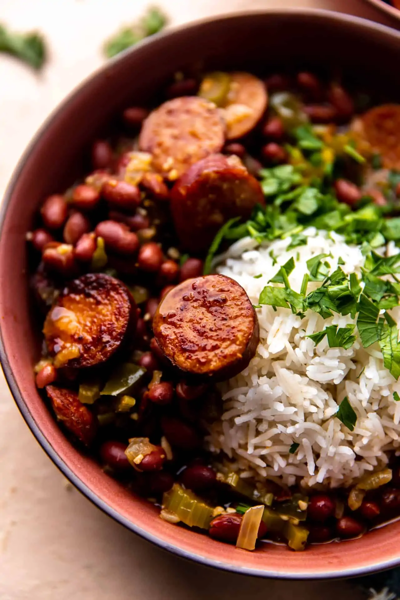 Up close view of red beans and sausage served with white rice and fresh parsley.
