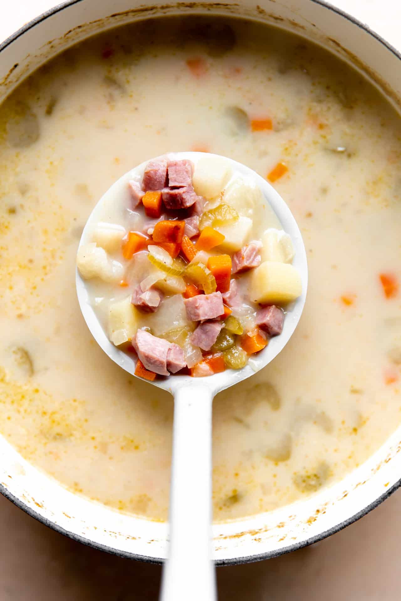 Spoon ladling up ham bone soup with bits of ham, potato and veggies in a creamy broth.