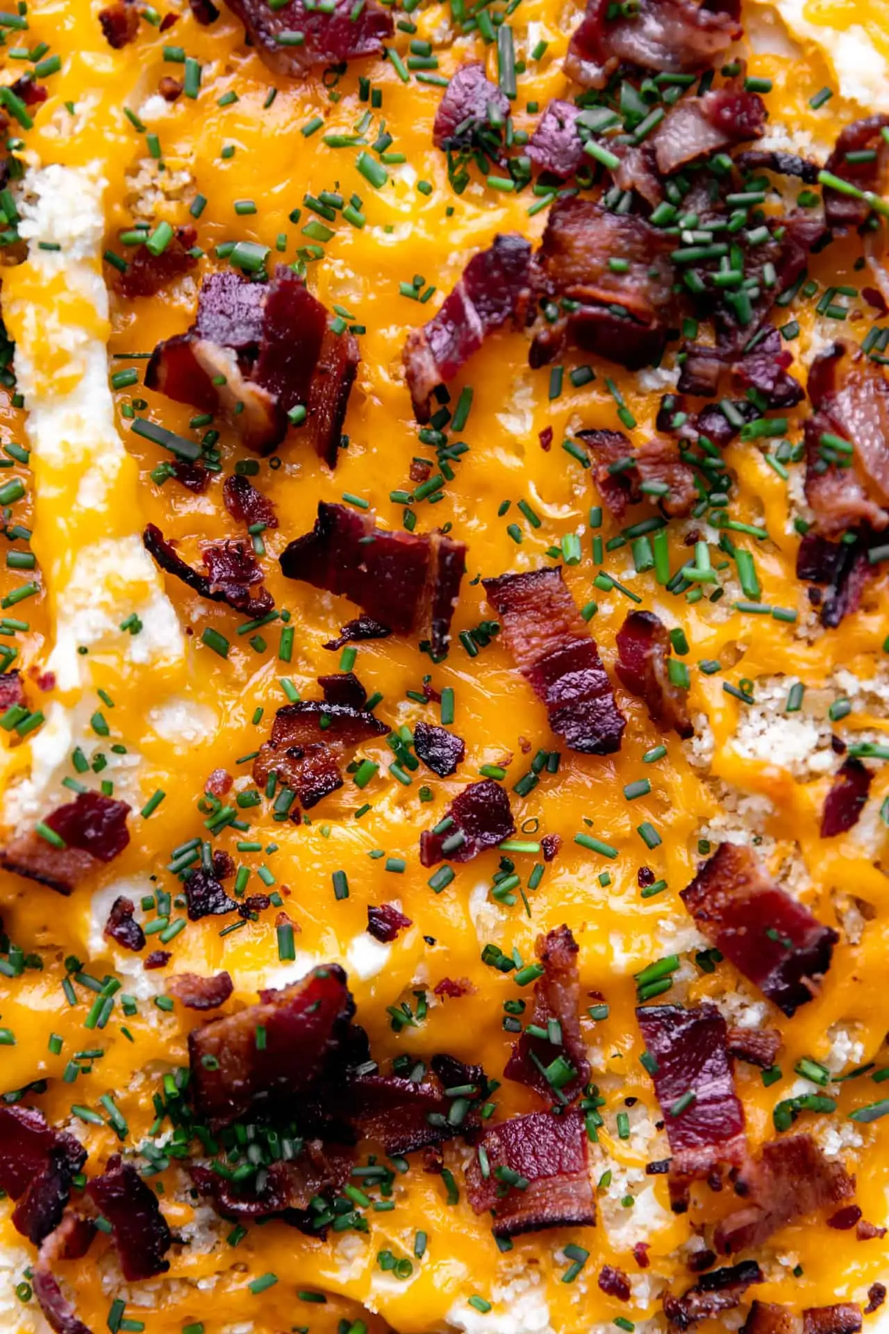 Toppings added to the mashed potato casserole after baking, showing melted cheese and crispy bacon with bits of fresh chives.