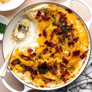 Dish of loaded potato casserole with servings removed by a spoon.