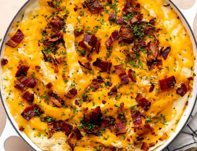 Round baking dish with baked mashed potato casserole, topped with melty cheese, crisp bacon and green chives.