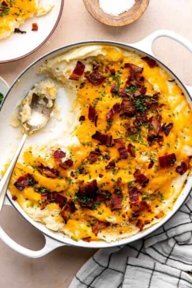 Dish of loaded potato casserole with servings removed by a spoon.