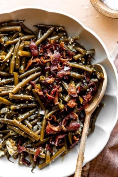 Bowl served with southern green beans topped with crispy bacon and a wooden spoon for serving.