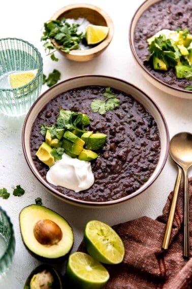 Bowl of black bean soup topped with diced avocado, sour cream and fresh cilantro.