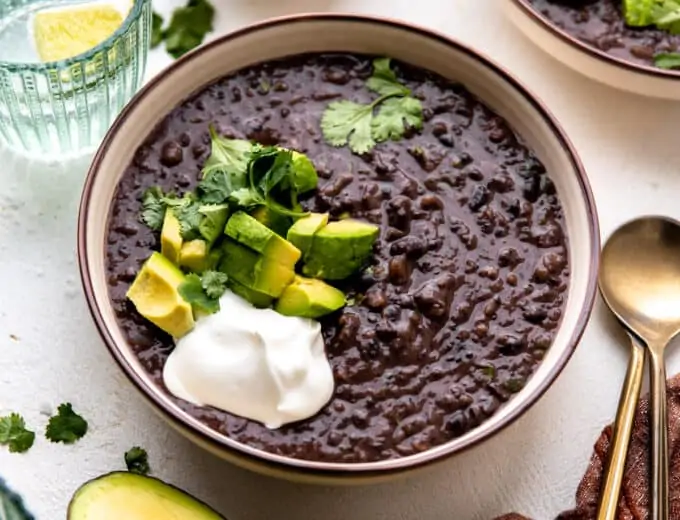 Bowl of black bean soup topped with diced avocado, sour cream and fresh cilantro.