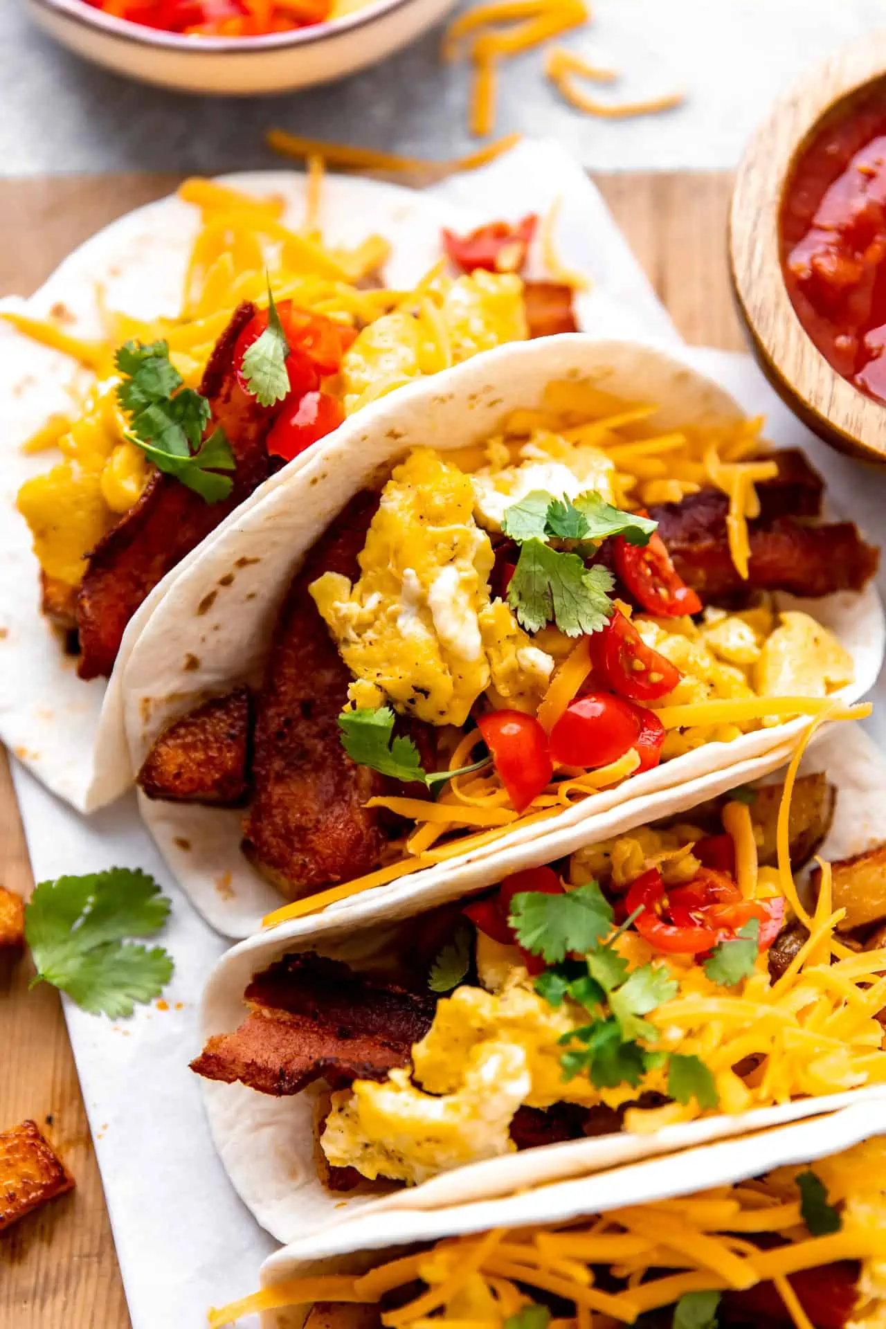 Up close view of breakfast tacos topped with shredded cheese, tomatoes and cilantro. 