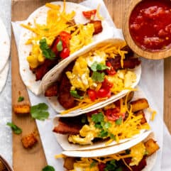 Tray of Breakfast tacos loaded with eggs, bacon and potatoes served with salsa.