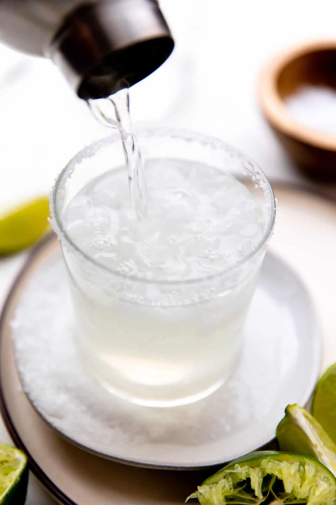 Shaker pouring lime margarita into a rocks glass filled with ice.