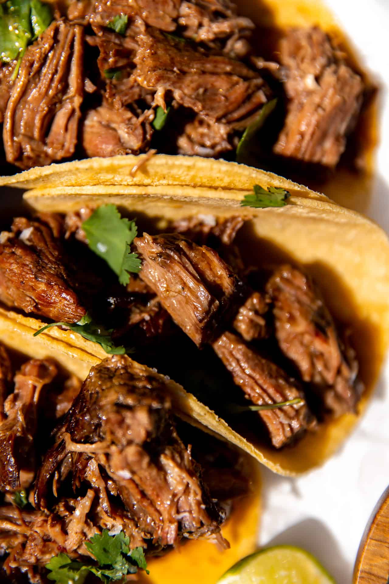 Shredded beef tacos on corn tortillas with cilantro and lime.
