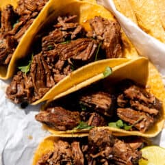 Shredded Beef tacos laid out on the counter in the sun with lime wedges and fresh cilantro.