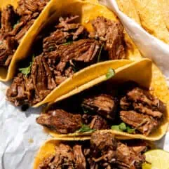 Shredded Beef tacos laid out on the counter in the sun with lime wedges and fresh cilantro.