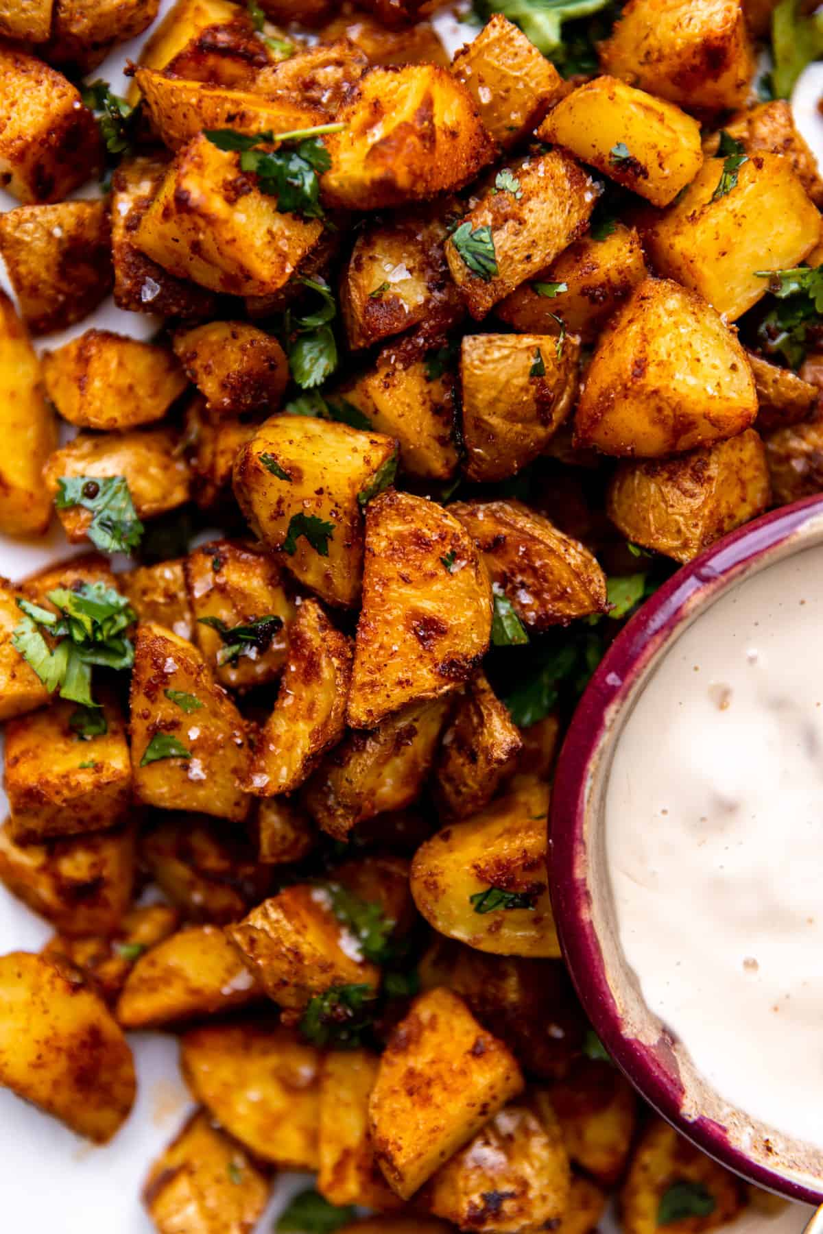 Up close view of roasted Tex Mex potatoes topped with cilantro and served with queso.