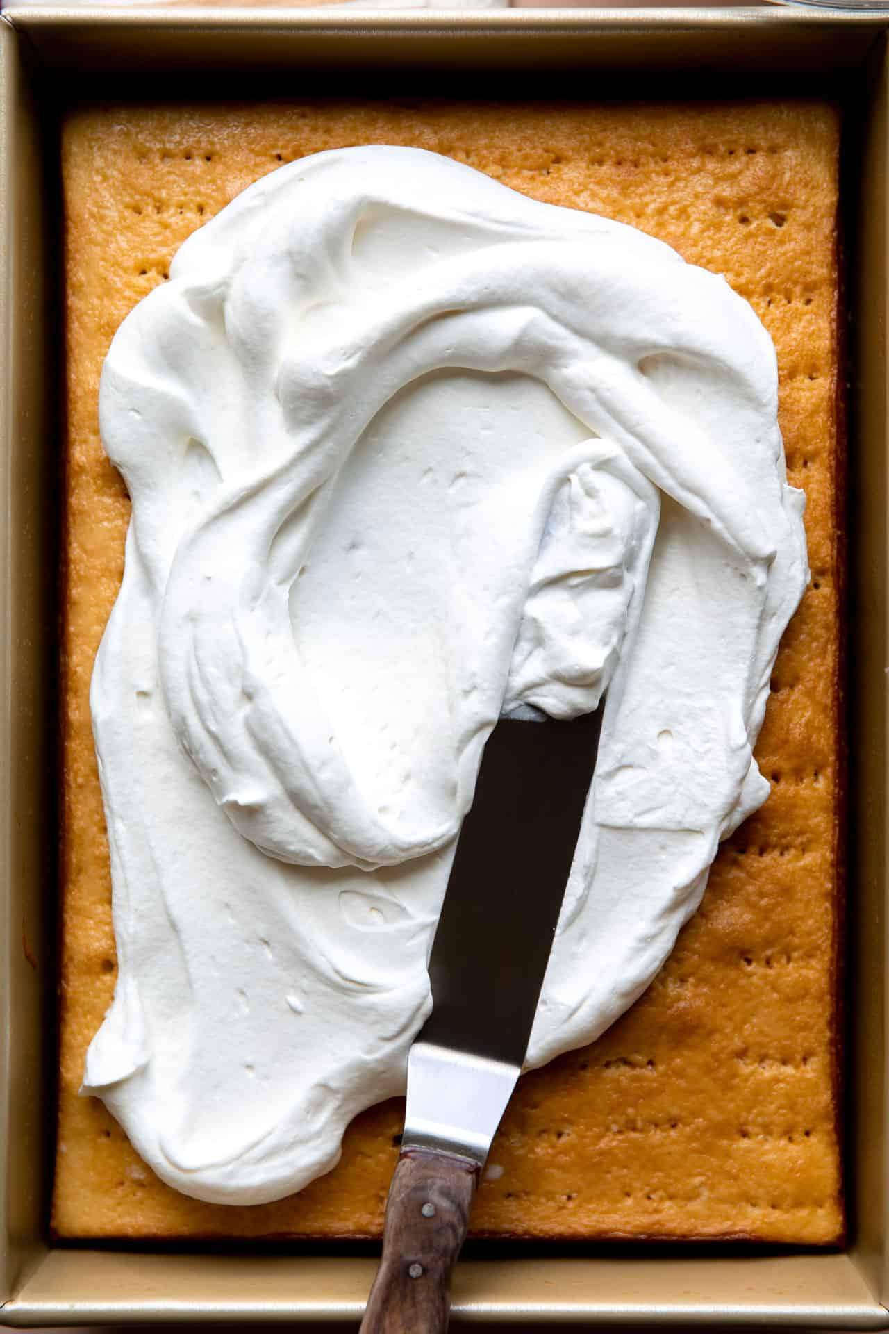 Soaked tres leches cake being topped with fluffy whipped cream. 