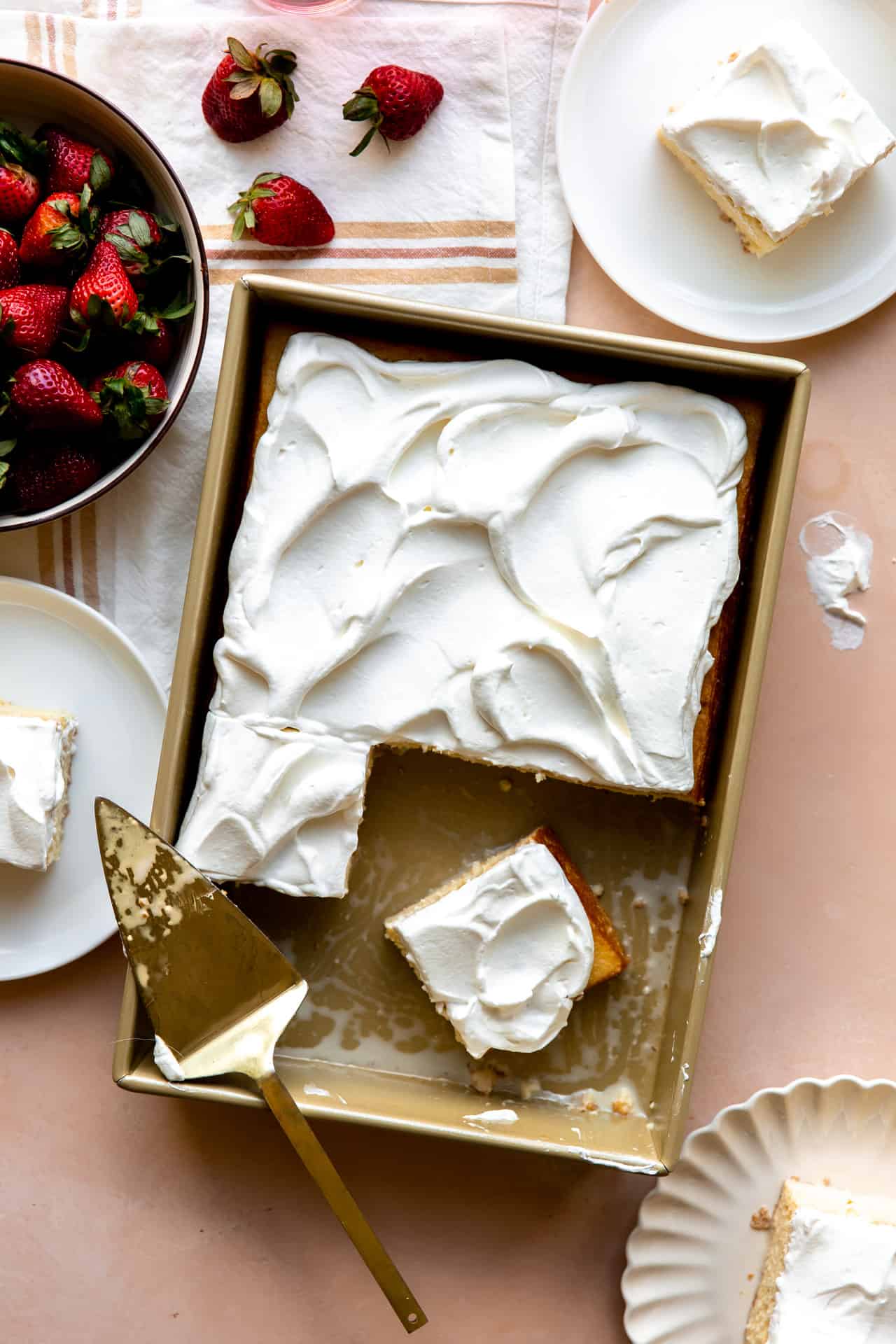 Tres Leches cake with slices cut out and being served with strawberries. 