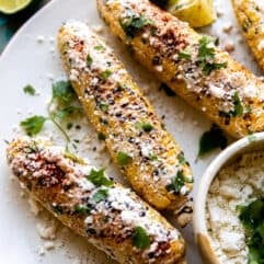 Plate of elotes served with extra crumbled cotija, lime wedges and fresh cilantro.