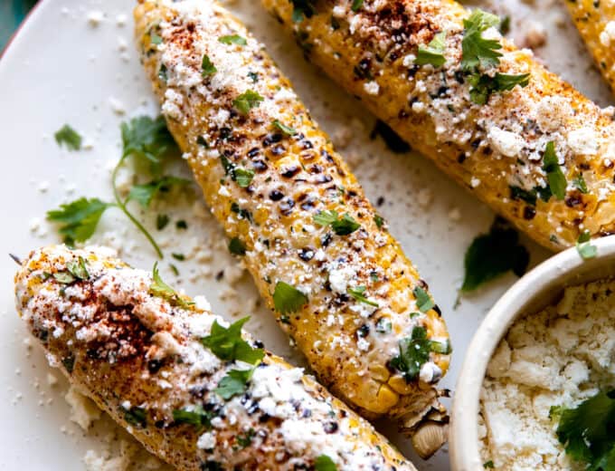 Plate of elotes served with extra crumbled cotija, lime wedges and fresh cilantro.