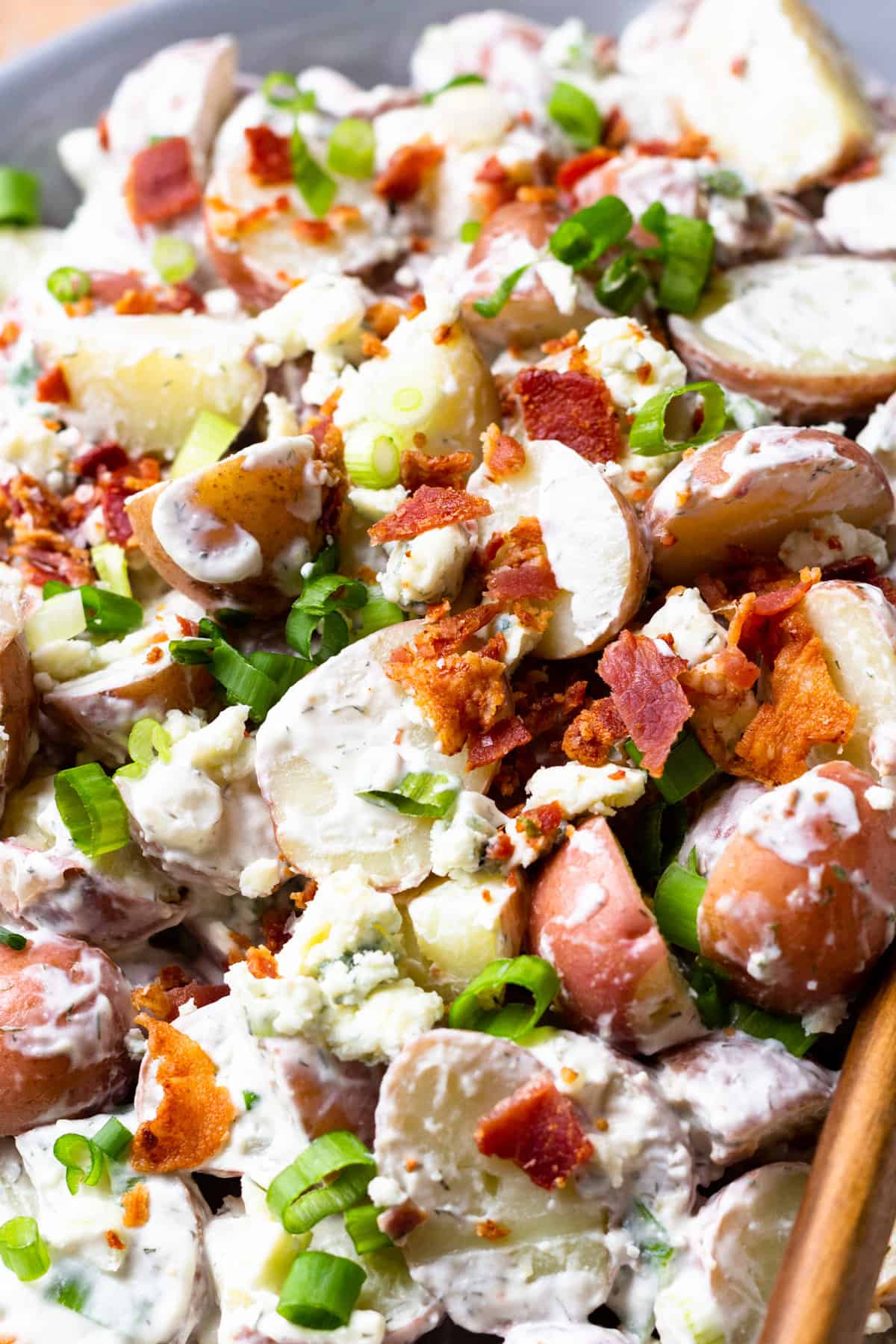 Up close view of red white and blue potato salad topped with crumbled bacon and green onion.