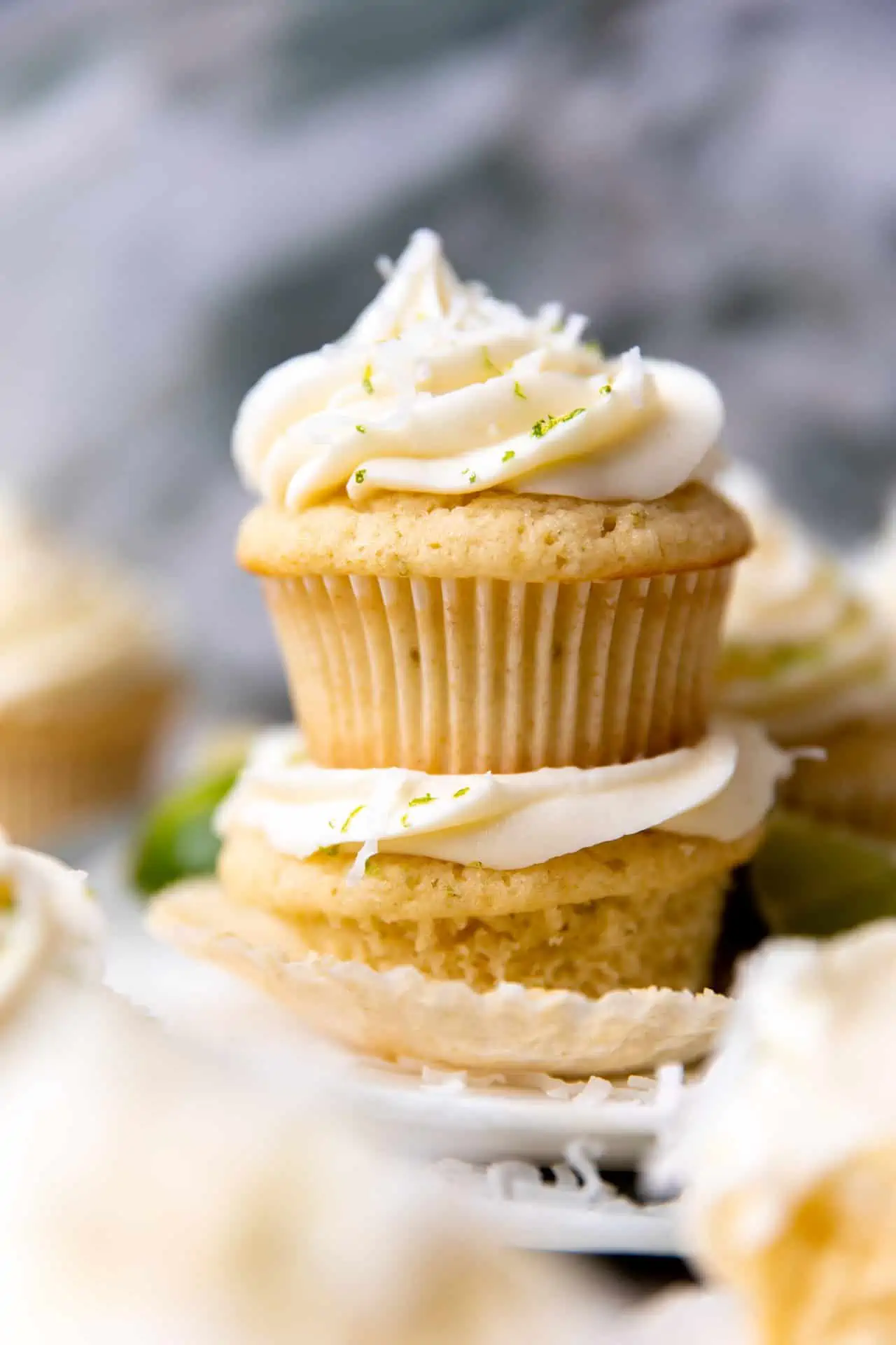 Stacked coconut lime cupcakes topped with coconut cream cheese frosting.