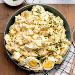 Bowl of creamy potato salad made with egg and dill pickle. Topped with sliced apart hard boiled egg.