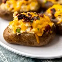 Twice baked potatoes served on a plate topped with melted cheese and crispy bacon.