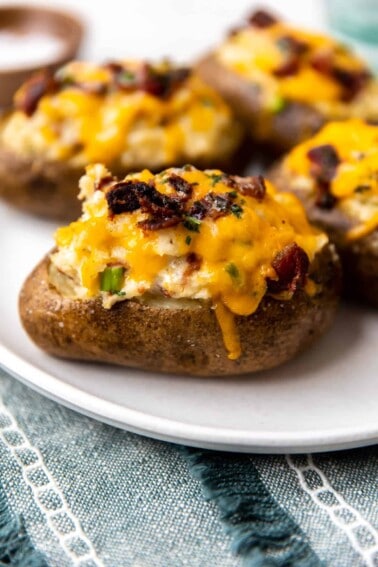 Twice baked potatoes served on a plate topped with melted cheese and crispy bacon.