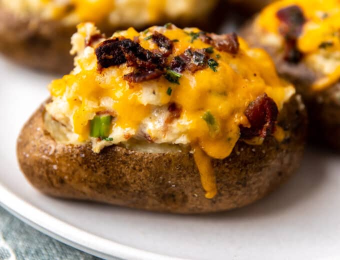 Twice baked potatoes served on a plate topped with melted cheese and crispy bacon.