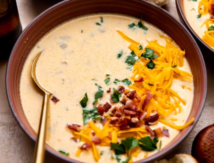 Bowl of beer cheese soup topped with shredded cheese and crumbled bacon.