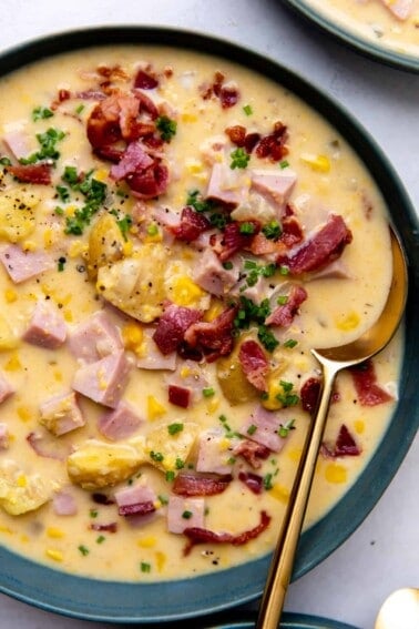 Up close of corn chowder in a bowl topped with bacon and herbs.