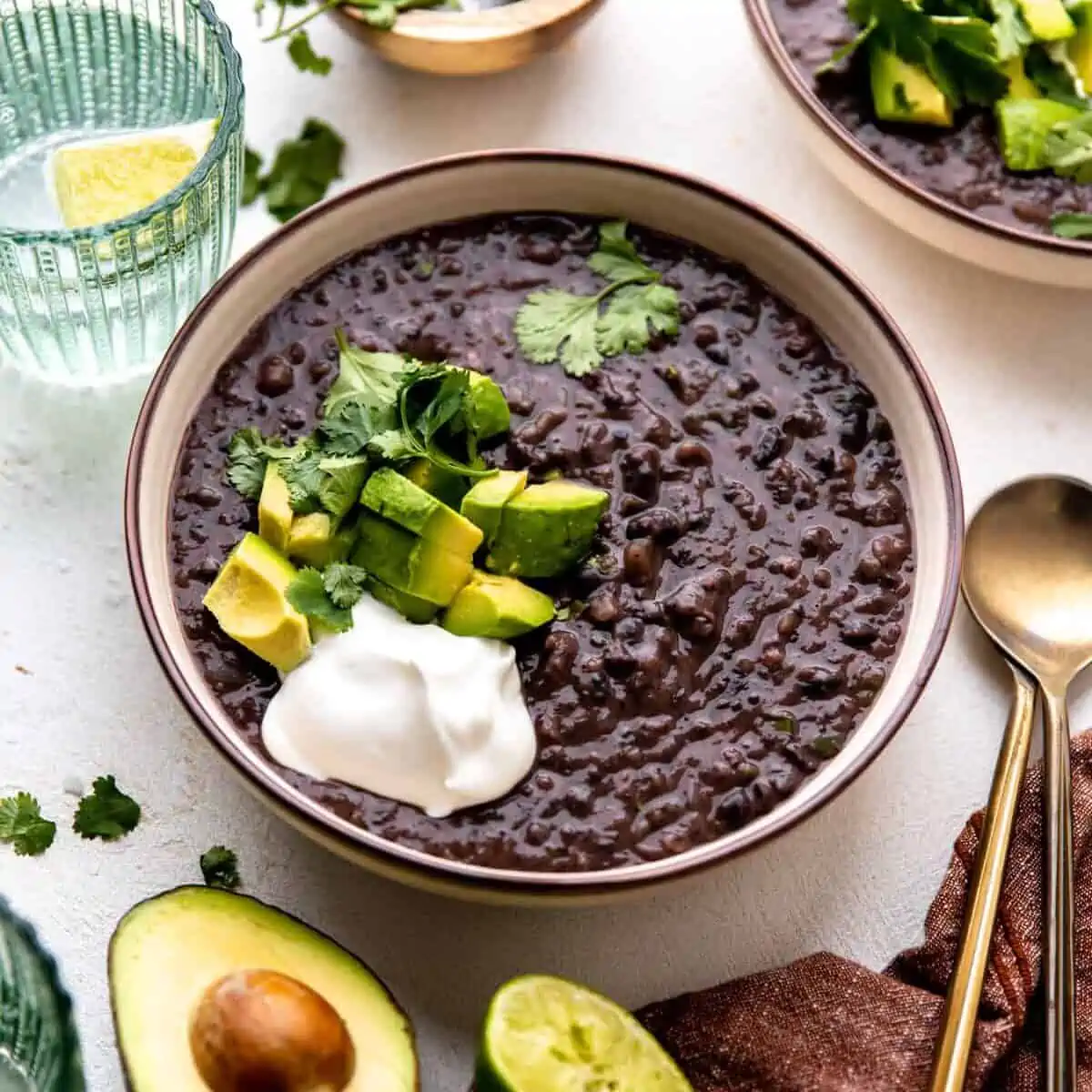 Bowl of black bean soup topped with diced avocado, sour cream and fresh cilantro.