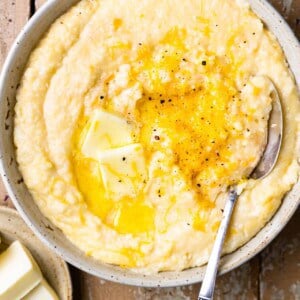 Bowl of cheese grits topped with melted butter and black pepper with a spoon.