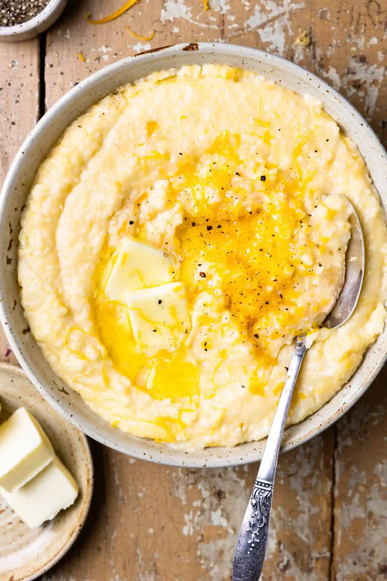 Bowl of cheese grits topped with melted butter and black pepper with a spoon.