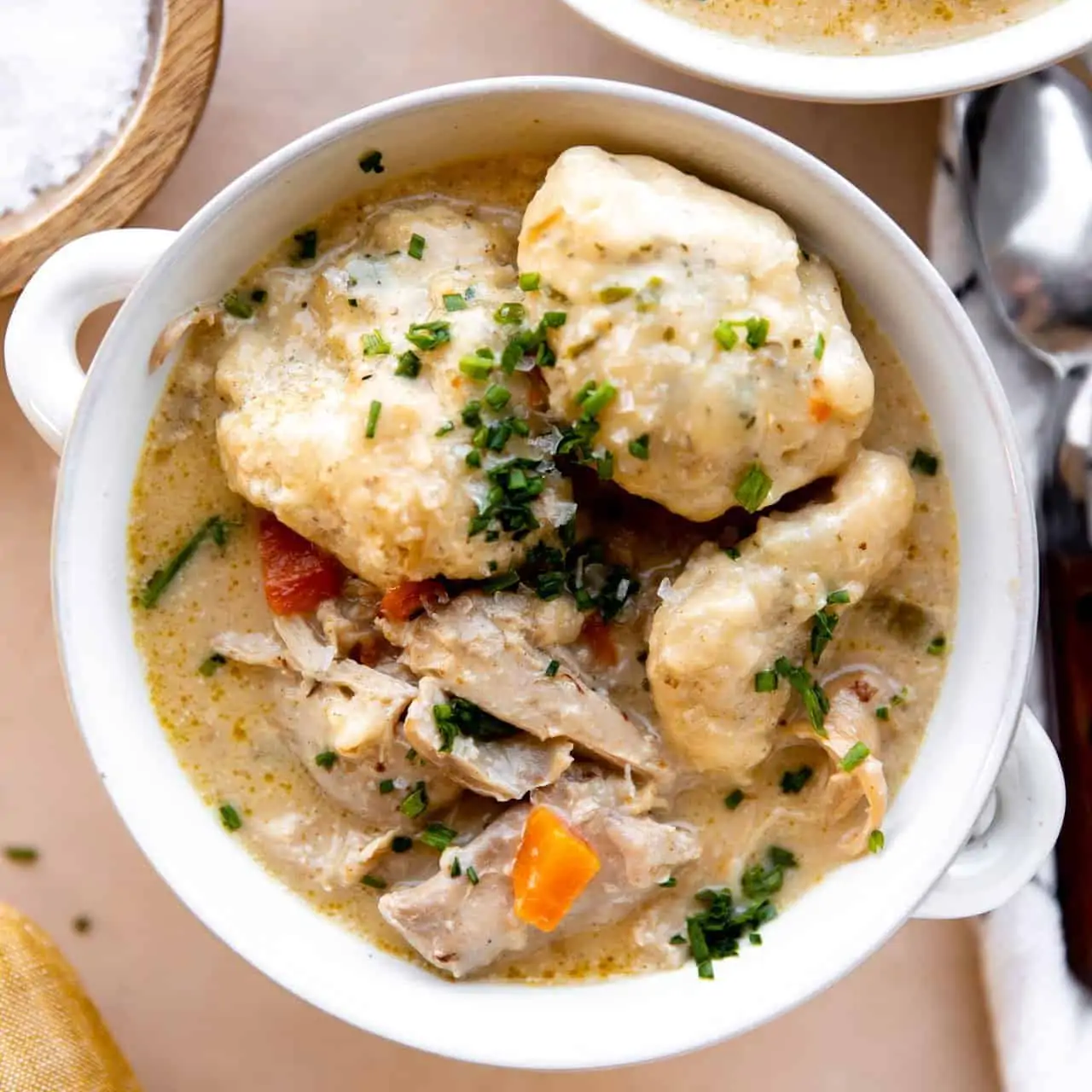 Bowl of creamy chicken soup topped with fluffy dumplings and topped with fresh herbs.