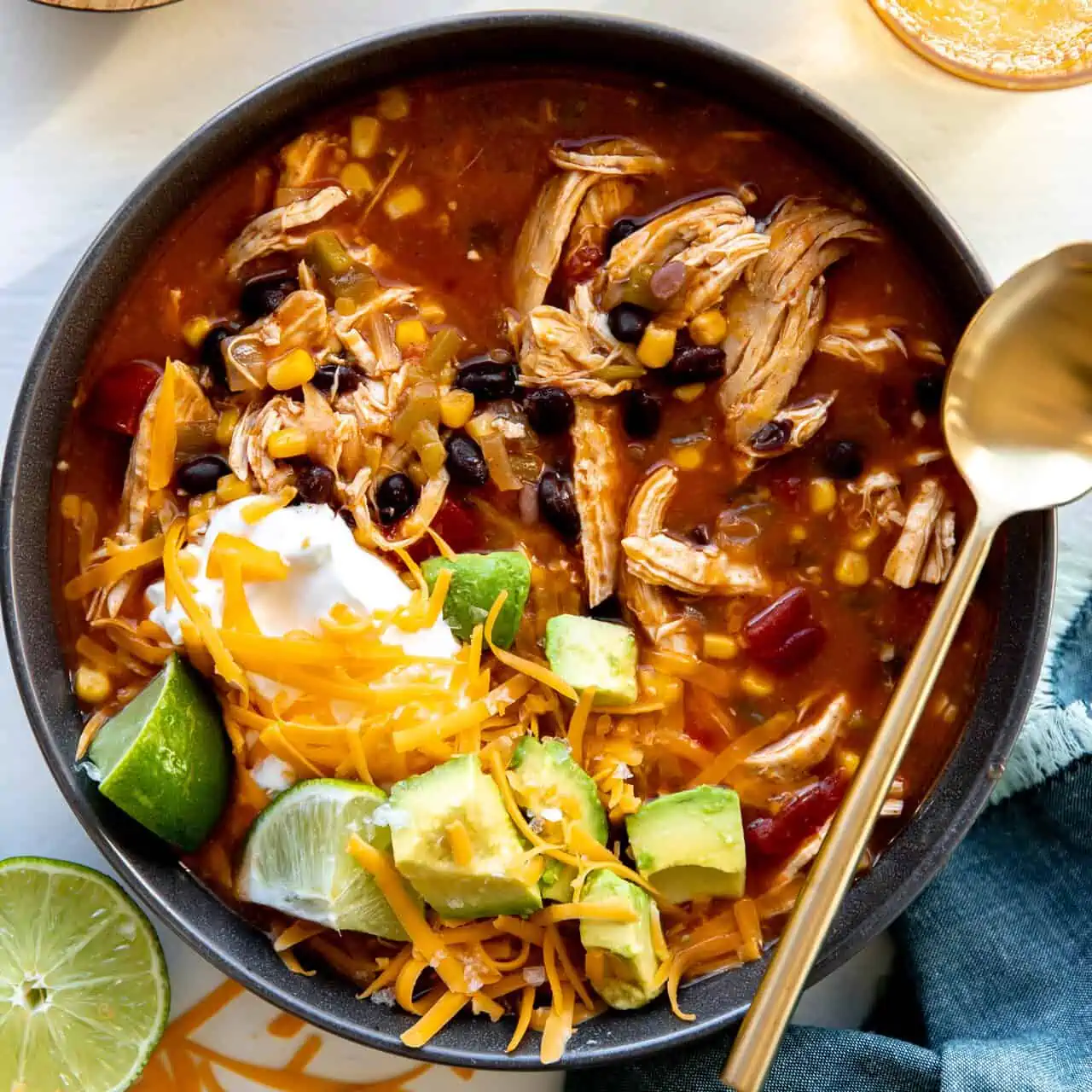 Bowl of chicken enchilada soup topped with cheese, sour cream and avocado.