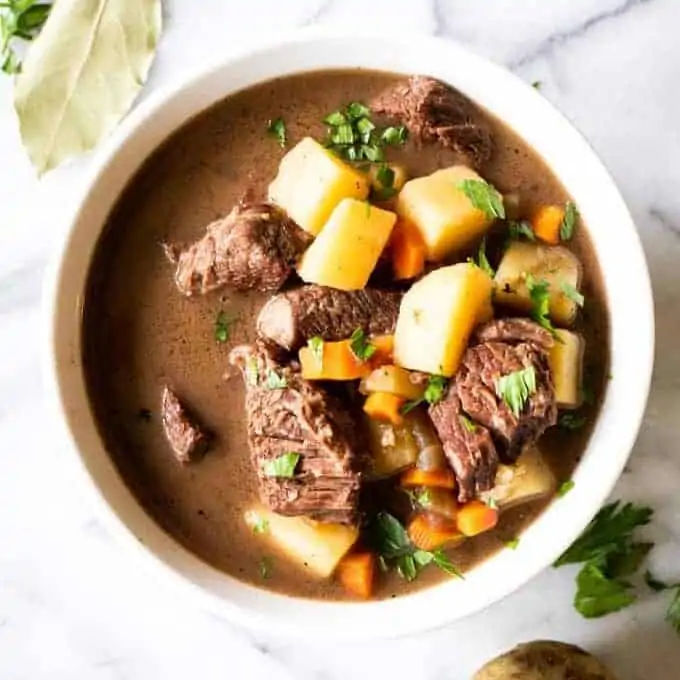 A bowl filled with beef stew, tender meat, flavorful gravy broth. Topped with fresh parsley.